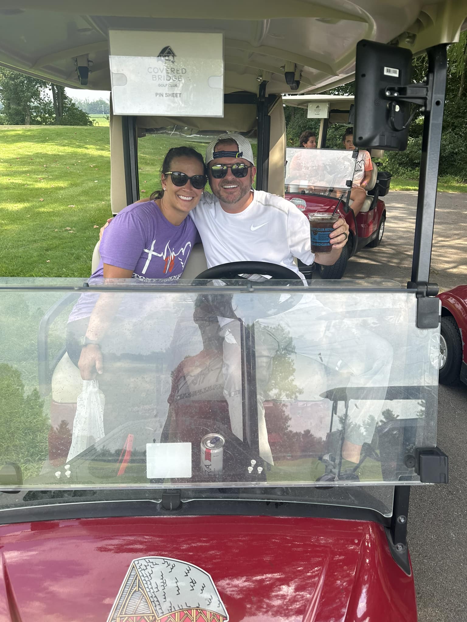 Two golfers sitting in a golf cart smiling at the camera.