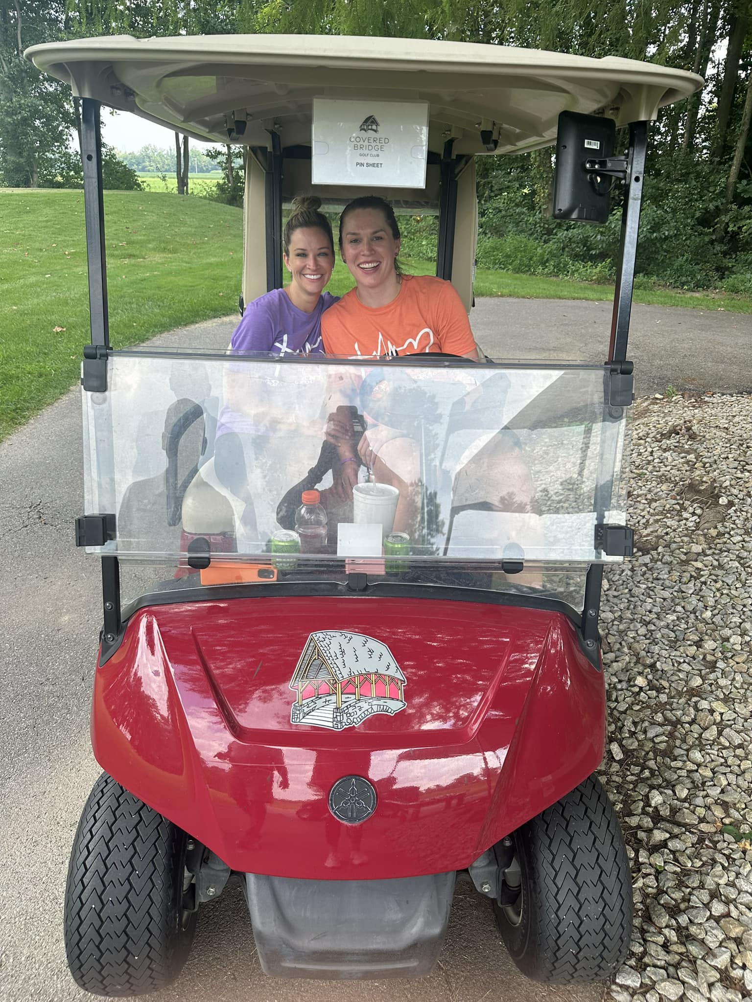 Golfers sitting in a golf cart smiling at the camera.
